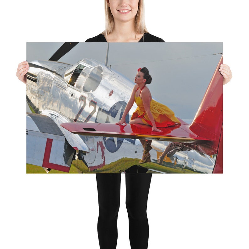 May include: A woman in a yellow and red dress sits on the wing of a silver and red airplane. The airplane has the number 22 on the side and a star on the wing.