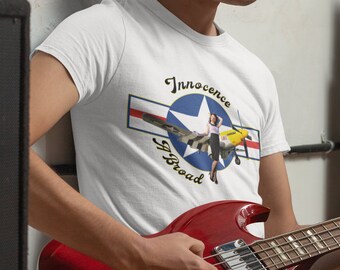 May include: A white t-shirt with a graphic of a pin-up girl sitting on a vintage airplane. The graphic includes the text "Innocence Abroad" and a star with red, white, and blue stripes.