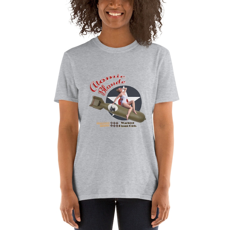 May include: A gray t-shirt with a vintage pin-up girl design. The design features a woman in a white swimsuit sitting on a bomb with the text "Atomic Blonde" above her. The text "Warbird Pinup Girls" is below her.