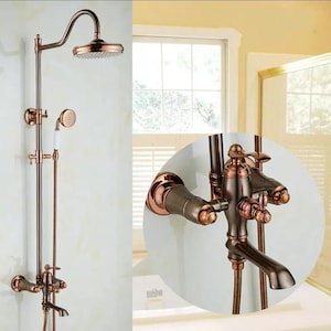 May include: A vintage-style shower fixture in bronze tones, featuring a curved showerhead, a handheld shower, and a faucet. The design includes decorative elements and a two-tone finish. The showerhead is circular, and the faucet has a spout and control knobs.