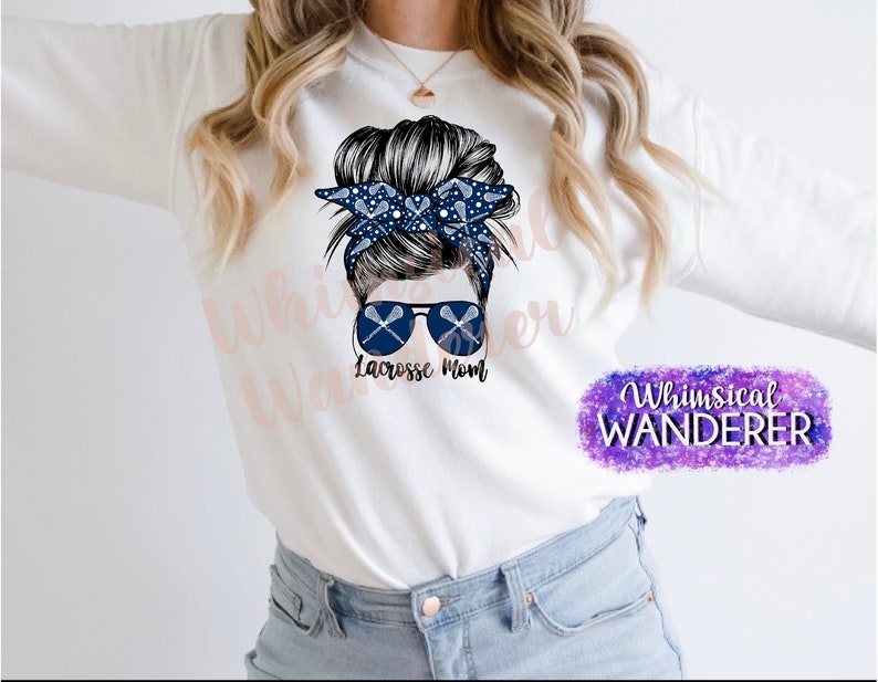 May include: White sweatshirt with a graphic of a woman with a messy bun, sunglasses, and lacrosse sticks. The text "Lacrosse Mom" is below the graphic. The text "Whimsical Wanderer" is in the bottom right corner.