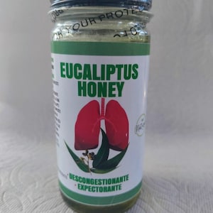 May include: A glass jar with a black lid filled with a green liquid. The label reads "Eucalyptus Honey" and features a red image of lungs and green eucalyptus leaves. The label also says "Decongestionante" and "Expectorante".