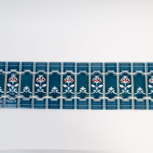 May include: A row of teal blue ceramic tiles with a white and red floral design. The tiles have a decorative border and are arranged in a repeating pattern.