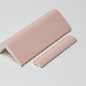 May include: Two pink ceramic tile trim pieces. One is a corner piece and the other is a straight piece.