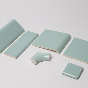 May include: A set of six light blue ceramic tile trim pieces, including a corner piece, a straight edge piece, a curved edge piece, and three square pieces.