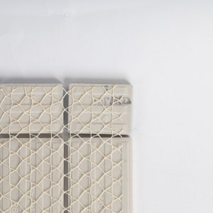 Puede incluir: Primer plano de un mosaico de azulejos con un patr&oacute;n de malla blanca. Los azulejos est&aacute;n dispuestos en una cuadr&iacute;cula y tienen un color gris claro.