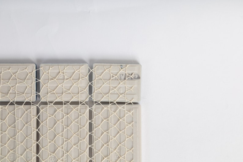 Puede incluir: Primer plano de un mosaico de azulejos con un patr&oacute;n de malla blanca. Los azulejos est&aacute;n dispuestos en una cuadr&iacute;cula y tienen un color gris claro.