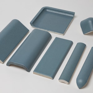 May include: A collection of blue ceramic tiles in various shapes, including corner pieces, rounded edges, and flat tiles. The tiles have a textured surface and a light blue color, suitable for a bathroom or kitchen project.