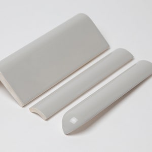 May include: Three white ceramic tile trim pieces. One is a corner piece and the other two are curved pieces.