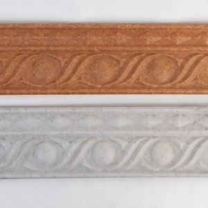 May include: Two decorative tile moldings, one in a light brown color and the other in a light gray color. Both moldings have a repeating pattern of a circle with a wavy design around it.