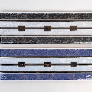 May include: Two ceramic tile samples with a striped pattern. The top tile has black and silver stripes with white accents. The bottom tile has blue and silver stripes with white accents.