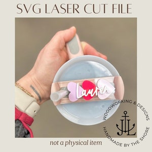 May include: A laser cut file for a personalized tumbler charm with the name "Lauren" and three pink and red hearts. The charm is designed to be attached to a tumbler lid.