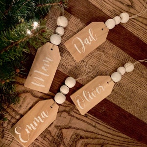 May include: Four wooden gift tags with white painted beads and twine. The tags are labeled "Mom", "Dad", "Oliver", and "Emma".