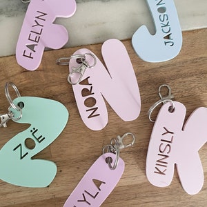 May include: Six colorful keychains with different names cut out of the shapes. The names are Faelyn, Jackson, Nora, Zoë, Kinsly, and Lyla. The keychains are made of a light pink, light blue, light green, and lavender material.