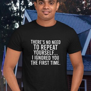 May include: Black t-shirt with white text: "THERE'S NO NEED TO REPEAT YOURSELF... I IGNORED YOU THE FIRST TIME." The shirt is worn by a person. A house and trees are visible in the background.