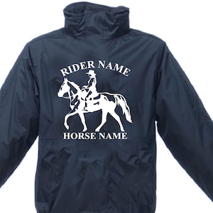 May include: Dark navy equestrian jacket featuring a white graphic of a rider on a horse. The jacket has a high collar and a zip closure. The text "RIDER NAME" and "HORSE NAME" are above and below the graphic.
