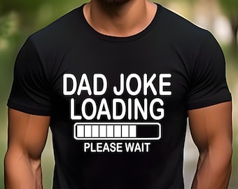 Puede incluir: Una camiseta negra de manga corta con el texto en blanco DAD JOKE LOADING, un gráfico de barra de carga debajo y el texto PLEASE WAIT debajo de la barra. La camiseta tiene un cuello redondo y un diseño de corte estándar.
