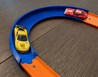 May include: A yellow toy car with a number 8 on the side is on a blue track. A red toy car is on an orange track. The tracks are connected to form a loop.