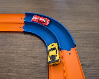 May include: A blue and orange Hot Wheels track set with two toy cars. One car is red and the other is yellow.