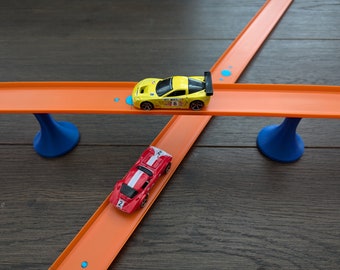 May include: Two toy cars on an orange track set. A yellow car is on the top track and a red car is on the bottom track. The track is supported by blue stands.