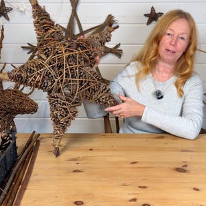 May include: A large, handcrafted star decoration made from woven twigs and pinecones. The star is brown and has a rustic, natural appearance. Other similar star decorations are visible in the background, suggesting a holiday or seasonal theme.