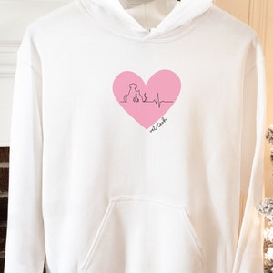 Peut inclure: Sweat-shirt à capuche blanc avec un graphique de cœur rose représentant un chien et un chat avec une ligne de battement de cœur et le texte "vet tech".