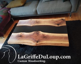 May include: A live edge coffee table with a black epoxy river running through the center. The table is made of walnut wood and has a natural, rustic finish. The table is sitting on a black rug.
