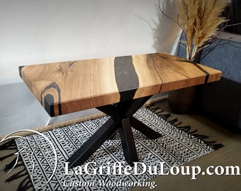 May include: A wooden coffee table with a black epoxy resin inlay and a black metal X-shaped base. The table is sitting on a black and white patterned rug.