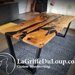 Peut inclure: Une table à manger en bois avec un incrustation de résine époxy noire. La table a un cadre en métal noir et est posée sur un tapis gris. La table est fabriquée par LaGriffeDuLoup.com, une entreprise de menuiserie sur mesure.