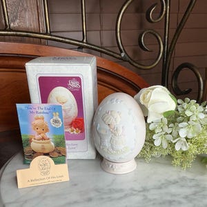 May include: A Precious Moments egg figurine with a girl design, displayed with its original box and a small card. The egg is light pink with a detailed relief design. The box features the text "You're The End Of My Rainbow".
