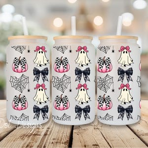 May include: Three glass tumblers with bamboo lids and straws. The tumblers feature a repeating pattern of pink and black checkered pumpkins, ghosts with pink bows, black bows, and spiderwebs. The text "C Dot Designs" is at the bottom.