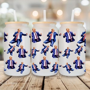 May include: Three white insulated tumblers with a repeating pattern of a man in a suit and red tie. The man is in various poses, including raising his arms in the air, pointing, and holding his hands on his hips. The tumblers are all the same size and shape, and they have a straw sticking out of the top.