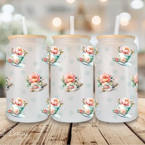 May include: Three frosted glass tumblers with a floral pattern of teacups and roses. The tumblers have a white background with light blue polka dots. Each tumbler has a straw.