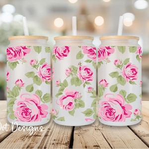 May include: Three glass tumblers with bamboo lids and straws. The tumblers are decorated with a pink rose floral pattern and the text "C Dot Designs" at the bottom left. The tumblers are sitting on a wooden surface.
