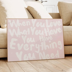 May include: A framed pink canvas with the text "When You Love What You Have You Have Everything You Need" in white lettering. The canvas is placed in front of a beige sofa and wooden table.