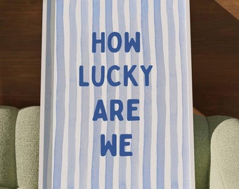 May include: A white framed print with blue and white stripes and the text "HOW LUCKY ARE WE" in blue.