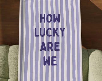 May include: A white framed print with purple text on a light blue and white striped background. The text reads "HOW LUCKY ARE WE".