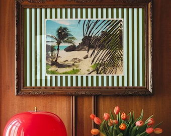 May include: A red mushroom-shaped table lamp with a scalloped edge sits on a wooden table. A framed picture with a beach scene and a vase of tulips are also on the table. The background is a wood-paneled wall.