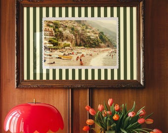 Pode incluir: Uma luminária de mesa vermelha em forma de cogumelo com abajur ondulado está sobre uma mesa de madeira. Acima, uma foto emoldurada de uma cidade costeira está pendurada em uma parede com painéis de madeira. Um vaso de tulipas.