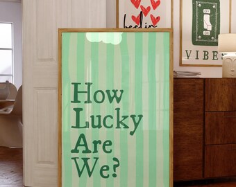 May include: A framed poster with the text "How Lucky Are We?" in green lettering against a light green and white striped background. Other framed art pieces are visible in the background.