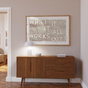 May include: A wooden sideboard with two doors and three drawers. A white lamp and a white bowl are on top of the sideboard. A framed print with the text "What if it all works out?" is hanging on the wall above the sideboard.