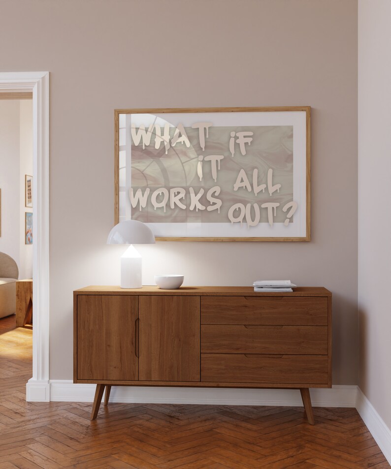 May include: A wooden sideboard with two doors and three drawers. A white lamp and a white bowl are on top of the sideboard. A framed print with the text "What if it all works out?" is hanging on the wall above the sideboard.