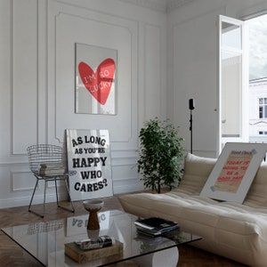 May include: A living room interior with a white couch, a glass coffee table, and three framed prints on the wall. The prints feature a red heart with the text "I'm so lucky", a black and white print with the text "As long as you're happy who cares?", and a white framed print with the text "Guest Check Today is going to be a good day!"
