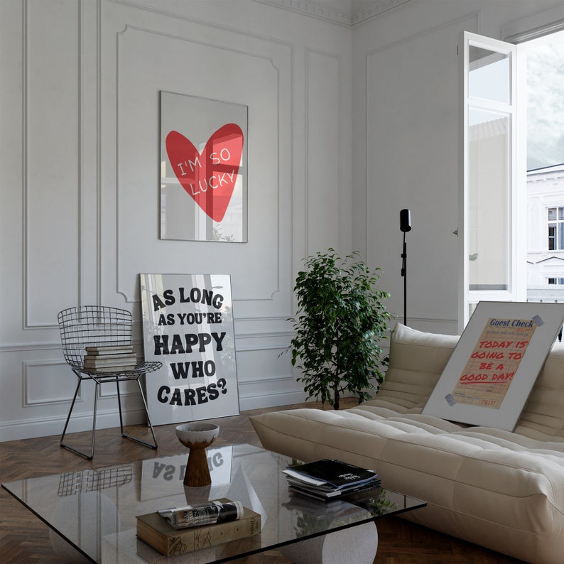 May include: A living room interior with a white couch, a glass coffee table, and three framed prints on the wall. The prints feature a red heart with the text "I'm so lucky", a black and white print with the text "As long as you're happy who cares?", and a white framed print with the text "Guest Check Today is going to be a good day!"