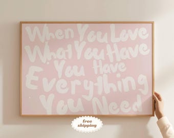 Peut inclure: Une affiche encadrée avec l'inscription blanche "When You Love What You Have You Have Everything You Need" sur fond rose. Le cadre est en bois brun clair. L'image est tenue par une personne.
