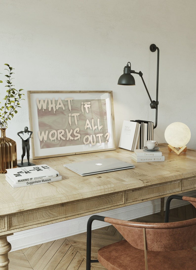 May include: A wooden desk with a laptop, books, a lamp, and a moon-shaped lamp. The wall behind the desk has a framed print with the text "What if it all works out?"