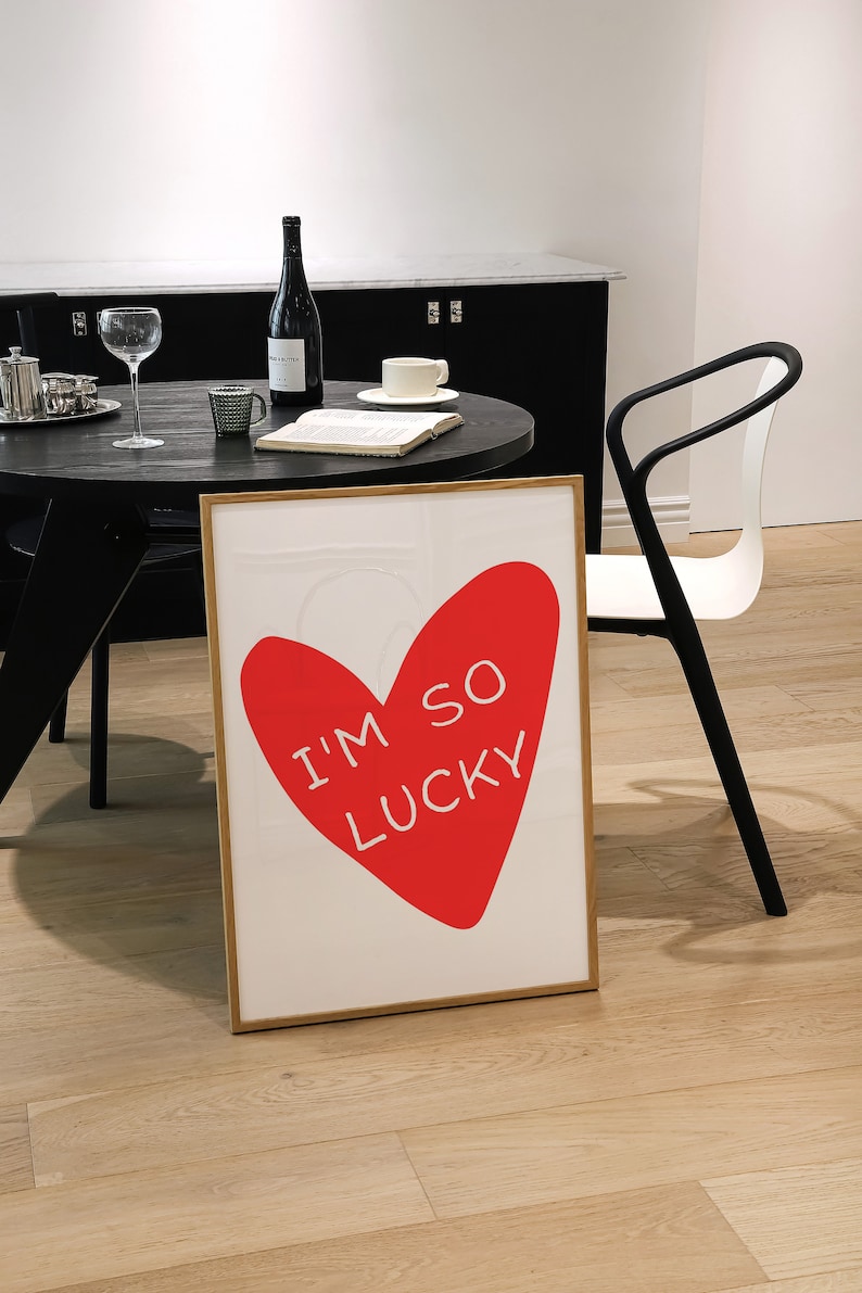 May include: A framed print with a red heart shape and the text "I'm so lucky" in white. The print is on a white background and has a wooden frame.