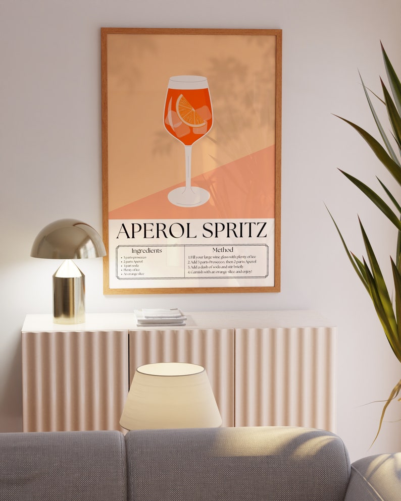 May include: A printable poster with an illustration of an Aperol Spritz cocktail. The poster has a peach background with a brown wood frame. The text on the poster reads "Aperol Spritz" and includes a list of ingredients and instructions for making the cocktail.