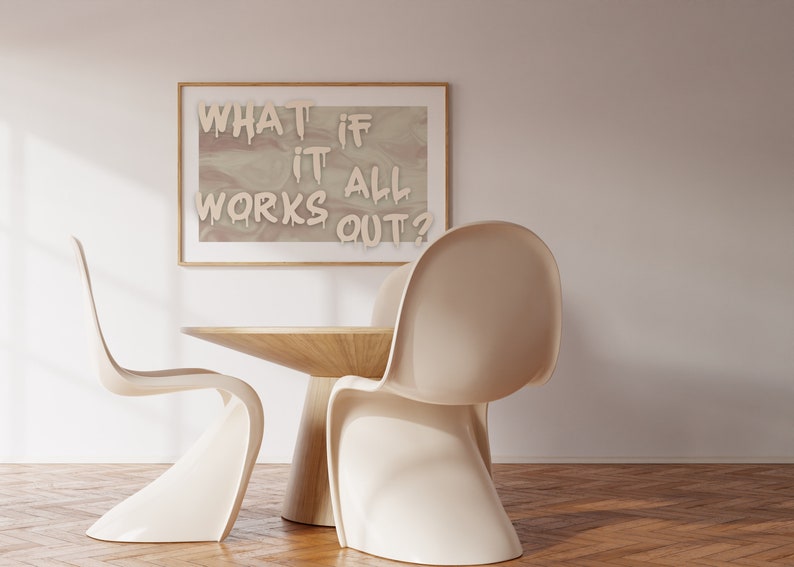 May include: A framed print with the text "WHAT IF IT ALL WORKS OUT?" in white paint on a beige background. Two white chairs and a wooden table are in the foreground.