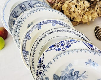 May include: A selection of white ceramic plates with blue patterns. The plates display various designs, including floral and geometric motifs. Some plates have scalloped edges and detailed borders. The plates are arranged in a neat display.